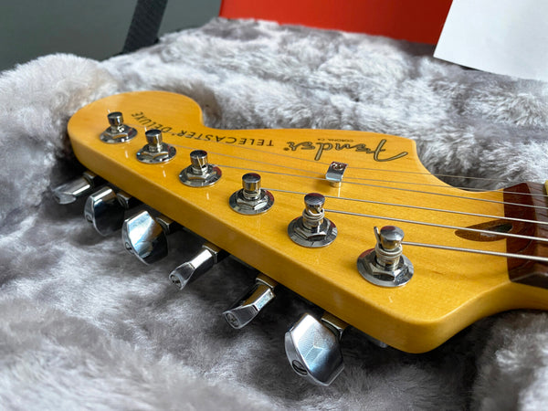 Close-up of Fender Telecaster Deluxe electric guitar headstock with tuning pegs in plush gray guitar case interior