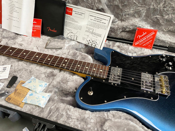 Fender electric guitar in blue burst finish with black pickguard, rosewood fretboard, and dual humbucker pickups displayed in gray plush guitar case with Fender manuals and accessories