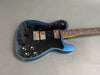 Electric guitar with metallic blue body, black pickguard, dual humbucker pickups, and rosewood fretboard on gray surface