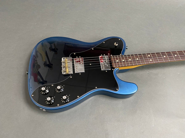 Electric guitar with metallic blue body, black pickguard, dual humbucker pickups, and rosewood fretboard on gray surface