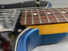Close-up view of electric guitar fretboard, steel strings, and shiny blue body with chrome pickups and screws.
