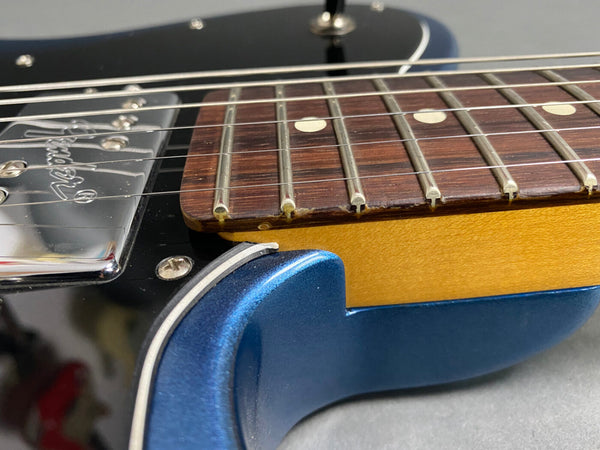 Close-up view of electric guitar fretboard, steel strings, and shiny blue body with chrome pickups and screws.