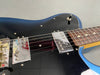 Close-up of blue electric guitar body showing black pickguard, chrome Fender pickups, switch, and rosewood fretboard with dot inlays