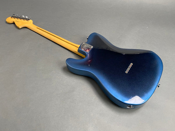 Electric guitar with metallic blue body and maple neck, back view on gray background