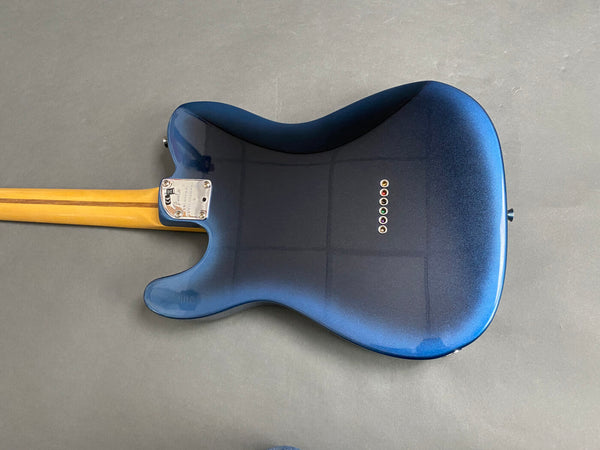 Back of electric guitar with metallic blue finish and wooden neck on grey background