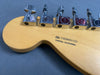 Close-up of Fender guitar headstock back showing chrome tuning pegs and serial number US20051123 with Corona, California stamp on maple wood
