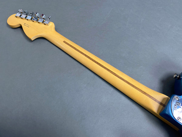 Maple guitar neck with walnut skunk stripe and chrome tuning pegs on electric guitar, blue body edge visible on gray background