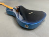 Back side view of glossy blue electric guitar with maple neck and chrome strap button on gray background
