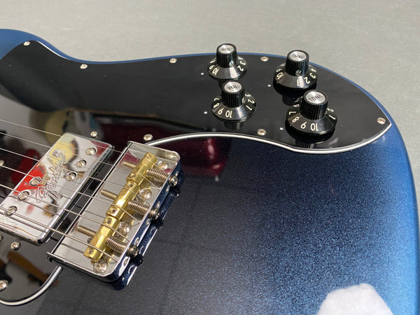 Close-up of black and blue electric guitar body showing Fender bridge, pickups, and black control knobs labeled volume and tone