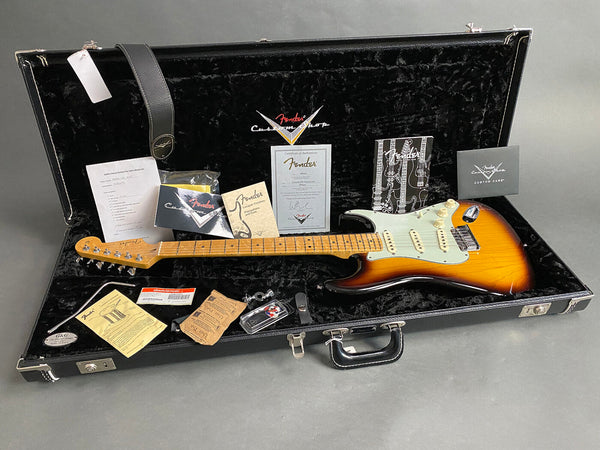 Fender Custom Shop sunburst electric guitar with maple neck inside black plush-lined hard case, including certificate of authenticity, Fender Custom Care booklet, warranty papers, coffee house guitars checklist, strap, and additional accessories.