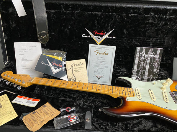 Fender Custom Shop sunburst electric guitar with maple neck and fretboard inside black plush guitar case, accompanied by Fender certificate of authenticity, Fender lacquer finishes care booklet, pre-sales checklist, guitar strap, guitar picks, strings, and user manuals.