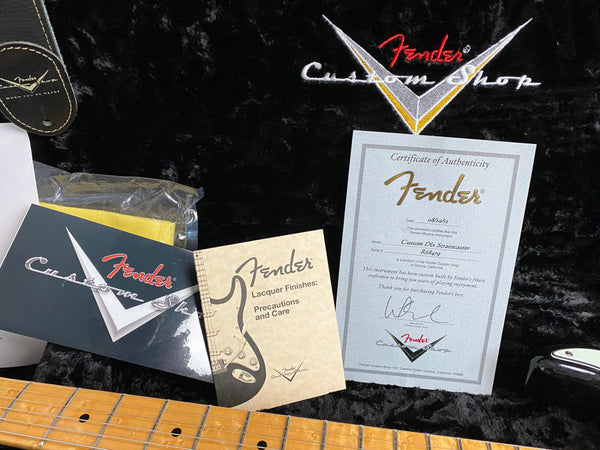 Fender Custom Shop certificate of authenticity for Custom DLx Stratocaster guitar, Fender Lacquer Finishes precaution and care booklet, black plush guitar case interior with Fender Custom Shop logo, and maple guitar neck.
