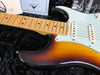 Close-up of Fender sunburst electric guitar body and maple neck with vintage white pickups resting on black plush guitar case lining with Fender Custom Shop certificate in the background