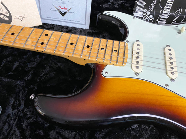 Close-up of Fender sunburst electric guitar body and maple neck with vintage white pickups resting on black plush guitar case lining with Fender Custom Shop certificate in the background