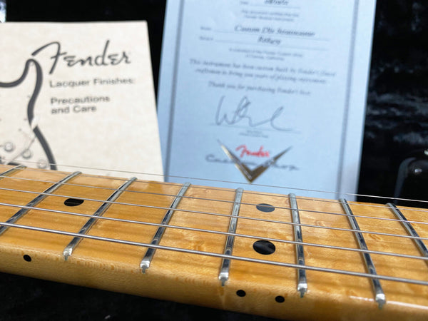 Close-up view of Fender guitar maple neck with strings and fretboard, Fender lacquer finishes care instructions and certificate of authenticity in the background