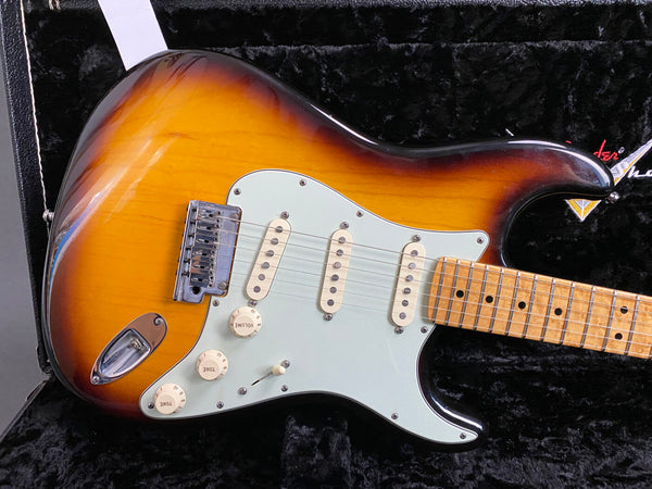 Sunburst electric guitar with maple fretboard and three single-coil pickups on black plush guitar case