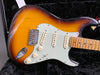 Sunburst electric guitar with white pickguard and three single-coil pickups in black plush-lined guitar case