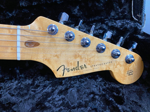 Close-up of light wood Fender Stratocaster guitar headstock with chrome tuning pegs on black plush guitar case interior