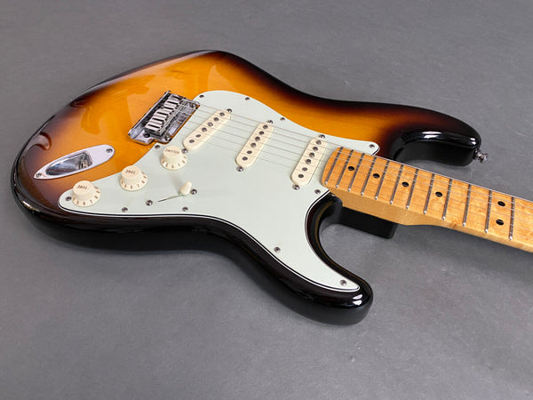 Sunburst electric guitar with maple fretboard and white pickguard, three single-coil pickups, and tone and volume control knobs on gray background