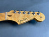 Close-up of Fender Stratocaster electric guitar headstock with natural wood finish and chrome tuning pegs on grey background