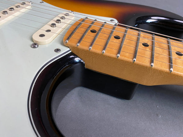 Close-up of electric guitar neck and body, showing maple fretboard, metal frets, string pickups, and sunburst finish guitar body.