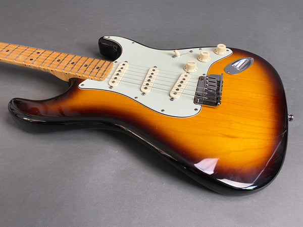Sunburst electric guitar with maple neck and white pickguard on gray background, featuring three single-coil pickups and vintage-style knobs.