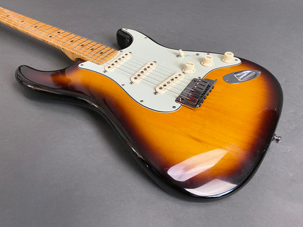 Sunburst electric guitar with maple neck and white pickguard on gray background, featuring three single-coil pickups and volume and tone knobs.
