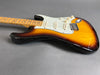 Sunburst electric guitar with maple neck and three single-coil pickups on gray background, close-up of body and neck.