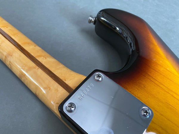Close-up of the back of a sunburst electric guitar body and maple neck with a four-screw neck plate showing serial number R68479