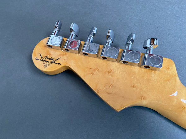 Close-up of Fender Custom Shop electric guitar headstock with chrome tuning pegs on a gray background