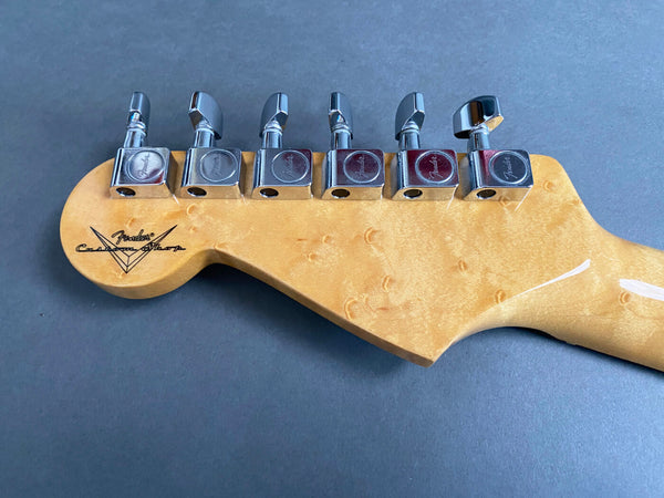 Close-up of Fender Custom Shop electric guitar headstock with six chrome tuning pegs on natural wood birdseye maple neck against gray background