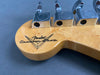 Close-up of Fender Custom Shop logo and chrome tuning pegs on natural wood guitar headstock