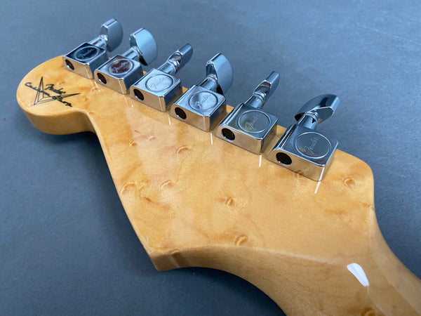 Close-up of Fender custom shop electric guitar headstock with chrome tuning pegs on a natural wood finish background