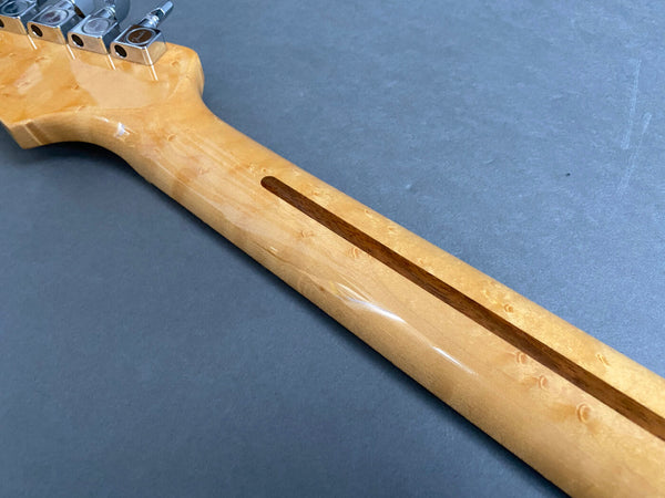 Close-up image of a guitar neck showing the smooth maple wood finish with a dark walnut skunk stripe and chrome tuning pegs on a gray background.