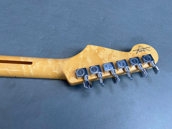 Maple guitar neck headstock with chrome Fender tuning pegs and guitar maker logo on gray background