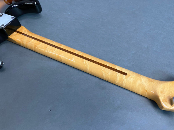 Close-up of birdseye maple guitar neck with skunk stripe on a gray background