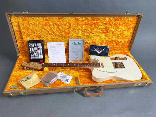Fender vintage white electric guitar in open brown hard case with orange plush interior, warranty and Fender booklet, cleaning cloth, and certificate of authenticity displayed