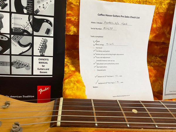 Close-up of Fender guitar neck showing frets and strings with Coffee House Guitars pre-sales checklist and Fender owner's manual in yellow plush guitar case interior.