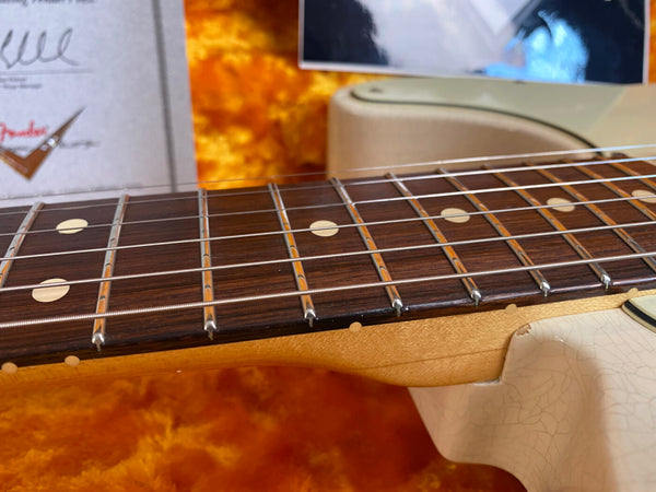 Close-up of rosewood fretboard with dot inlays and metal frets on a vintage electric guitar neck with a cracked cream finish body background