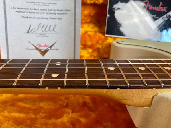 Close-up of Fender guitar rosewood fretboard with dot inlays and certificate of authenticity in background placed on orange plush guitar case interior