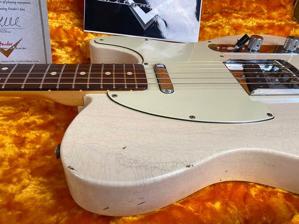 Close-up of vintage white electric guitar body with crackled finish, rosewood fretboard, and chrome bridge on orange plush guitar case lining