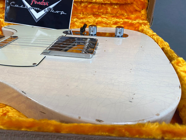 Close-up of vintage white Fender Telecaster electric guitar body with visible aging and wear, resting in orange plush-lined case with Fender Custom Shop card visible in background