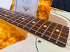 Close-up of electric guitar fretboard with white dot inlays and aged cream body in orange plush case with Fender guitar strings in background