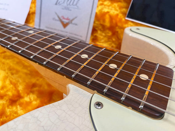 Close-up of electric guitar fretboard with white dot inlays and aged cream body in orange plush case with Fender guitar strings in background