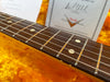 Close-up of rosewood guitar fretboard with metal frets and dot inlays, background with Fender certificate and orange plush guitar case interior