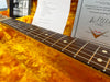 Close-up of Fender Custom Shop guitar rosewood fretboard with dot inlays and strings, resting on plush orange case lining with Fender Custom Shop certificate in background
