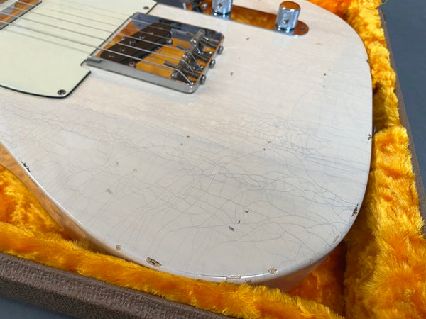 Close-up of vintage white electric guitar body with cracked lacquer and chips, resting in orange plush-lined guitar case