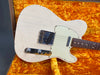Close-up of vintage white electric guitar body with aged finish and chrome hardware on orange plush guitar case lining