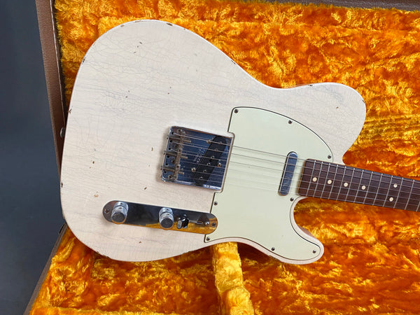 Close-up of vintage white electric guitar body with aged finish and chrome hardware on orange plush guitar case lining