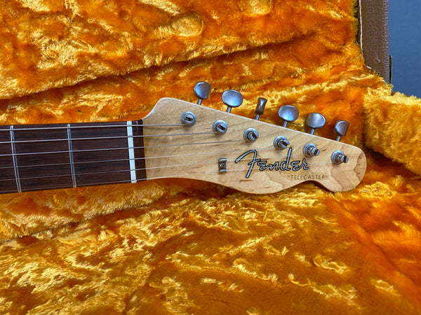 Close-up of Fender Telecaster guitar headstock with tuning pegs and rosewood fretboard resting on bright orange plush interior of guitar case.